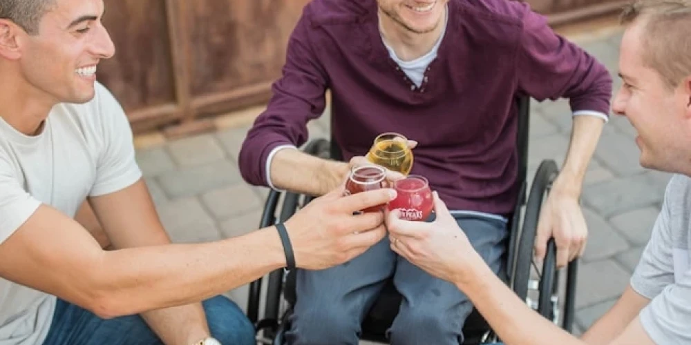 Ein Rollstuhlfahrer und zwei weitere Personen stoßen an mit ihren Drinks