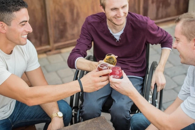 Ein Rollstuhlfahrer und zwei weitere Personen stoßen an mit ihren Drinks