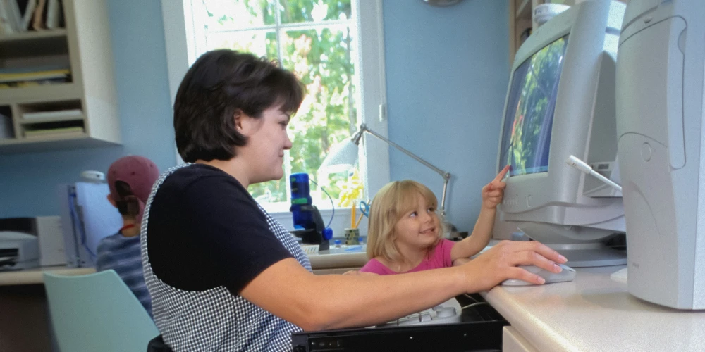 Frau im Rollstuhl bedient einen Computer, ein Kind steht daneben